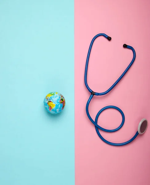 The problem of the global pandemic. Stethoscope and globe on pink blue background. Global epidemic. Top view