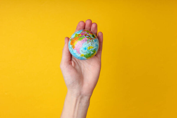 Globe in a female palm on a yellow background. Planet earth care concept