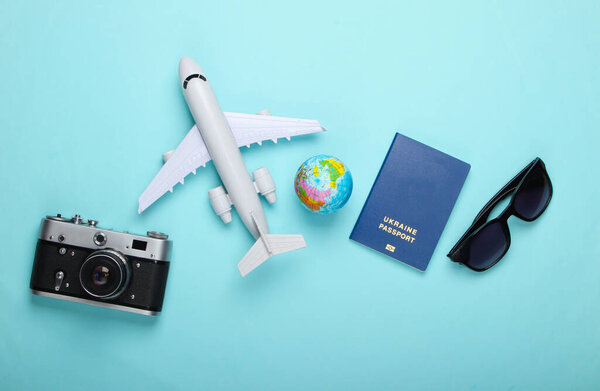 Tourism and travel concept. Globe, passport, passenger plane figurine, sunglasses and camera on blue pastel background. Top view. Flat lay