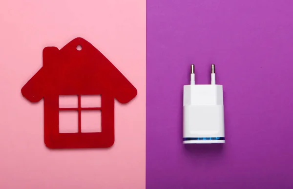 Smart house concept. Figurine of house with charger on a pink-purple background. Top view