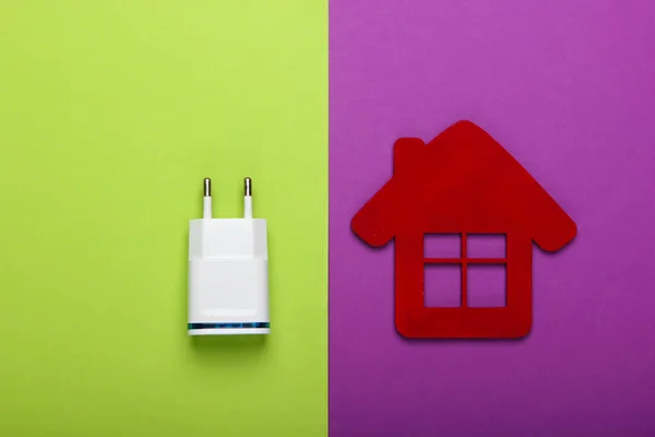 Smart house concept. Figurine of house with charger on purple green background. Top view