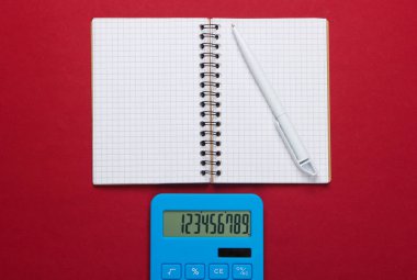 Kırmızı arka planda not defteri olan hesap makinesi. Eğitim süreci. Üst Manzara. Düz yatıyordu
