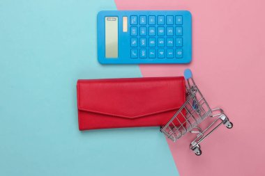 Aile bütçesini yönet. Alışveriş maliyetleri. Mavi hesap makinesi, deri cüzdan, pembe mavi pastel arka planda alışveriş arabası. Üst görünüm
