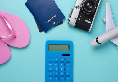 Turizm ya da tatil beldesinin maliyetinin hesaplanması. Düz yatıyordu. Yolcu uçağı, hesap makinesi, parmak arası terlik, pasaport, mavi arka planda kamera figürü. Yaz dönemi. Üst görünüm