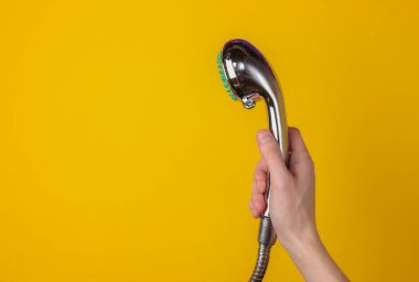 Sarı arka planda duş başlığını tutan el..