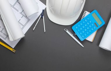 İnşaat kaskı, plan ruloları, proje planı ve gri arka planda hesap makinesi. Bir ev inşa etmenin maliyetinin hesaplanması. Üst Manzara. Düz yatıyordu