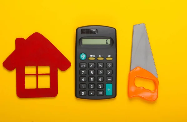 Calculation of the cost of building a house or repair. House figurine, calculator and toy saw on yellow background. Top view