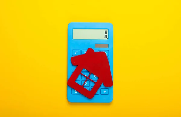 Calculation of the cost of rental housing. Red house figurine, calculator on yellow background. Top view