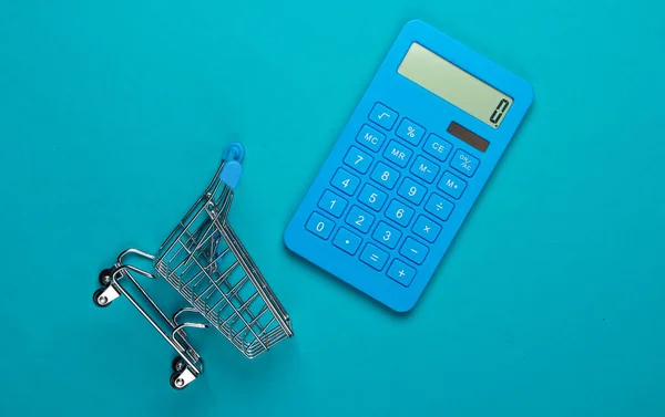 Calculation of costs for shopping, purchases in the supermarket. Calculator and shopping trolley on blue background. Top view. Minimalism