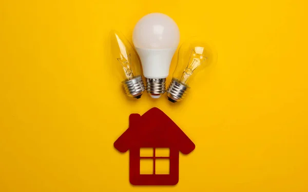 Energy saving concept. House figurine and light bulbs on yellow background. Top view