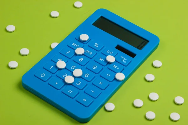 Calculation of the cost of medical expenses. Calculator and pills on green background. Top view. Minimalism