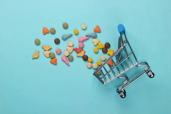 Veterinary tablets of vitamins with different shapes for cats and shopping trolley on blue background