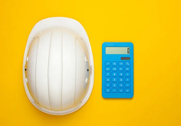 Engineering construction safety helmet and calculator on yellow background. Calculation of the cost of repair or building a house. Top view. Flat lay