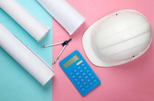 Engineering construction safety helmet, drawing rolls, compass and calculator on pink blue pastel background. Calculation of the cost building a house. Top view. Flat lay
