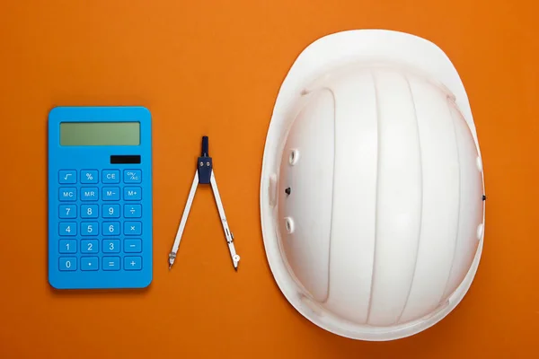 Engineering construction safety helmet, compass and calculator on orange background. Calculation of the cost of repair or building a house. Top view. Flat lay