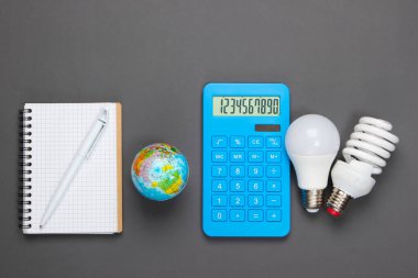 Enerji tasarrufu analizleri. Ampullü hesap makinesi, defter, gri arka planda küre. Üst görünüm
