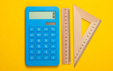 Hesap makinesi ve tahta cetvel, sarı arka planda üçgen. Eğitim konsepti. Üst görünüm