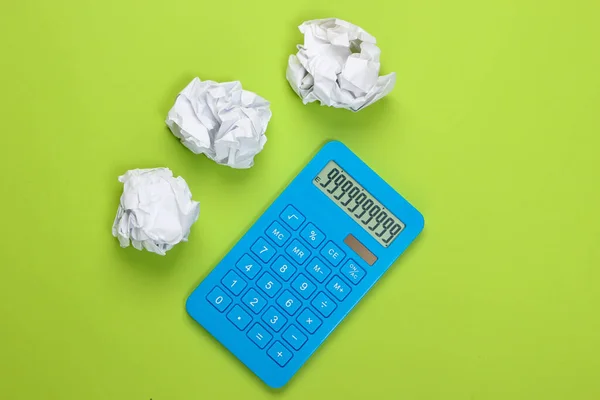 Blue calculator with crumpled balls of paper on green background. Top view