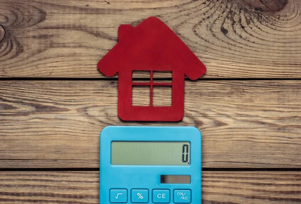 Calculation of the cost of renting or buying house. Calculator with red figure of house on wooden background. Top view