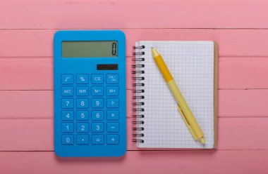 Pembe ahşap arka planda not defteri olan mavi hesap makinesi. Üst görünüm