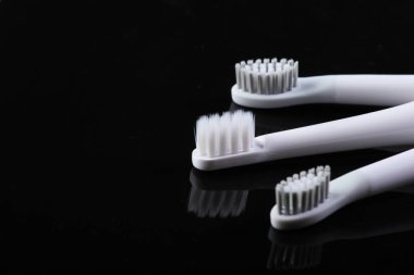 Siyah yansıtıcı arka planda üç diş fırçası.