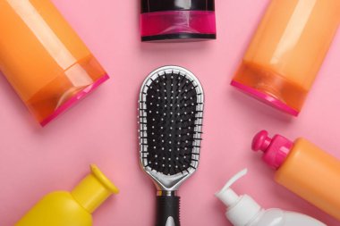 Pembe pastel arka planda şampuan şişeli saç fırçası. Saç bakımı. Hijyen. Güzellik düzlüğü. Üst görünüm