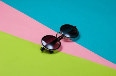 Renkli kağıttan bir arka planda yuvarlak güneş gözlüğü. Minimalizm