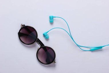 Beyaz arka planda yuvarlak gözlükler ve elektrikli kulaklıklar.