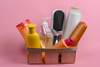 Kozmetik ürünleri şişeleri, şampuanlar, pembe pastel arka planda ahşap bir sepetin içinde tarak. Güzellik ürünleri