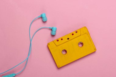 Pembe pastel arka planda kulaklıklı Retro ses kaseti. 80 'ler. Üst Manzara. Minimalizm.