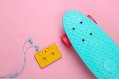 Kruvazör tahtası ve retro ses kaseti, pembe pastel arka planda kulaklıklar. 80 'ler. Üst Manzara. Minimalizm.