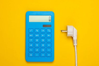 Sarı arka planda elektrik prizi olan bir hesap makinesi. Enerji tüketiminin maliyetlerinin hesaplanması. Üst görünüm