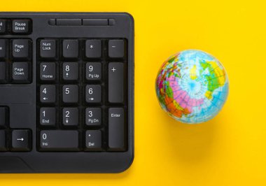 Sarı arka planda bilgisayar klavyesi ve küre. Çalışma alanı. Üst görünüm