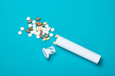 Mavi arka planda farklı haplarla dolu bir şişe..