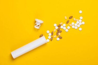 Sarı arka planda farklı haplar olan şişe..