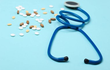 Farklı haplarla dolu bir şişe ve mavi arka planda steteskop. Tıbbî kardiyolojik hayat. Üst görünüm