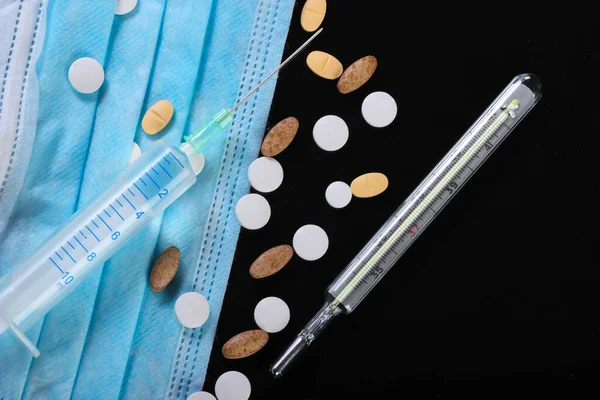 Medical still life. Syringe, thermometer, medical mask, pills. Black background. Diagnosis, protection and treatment of covid-19. Global pandemic