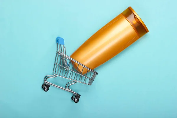 Mini supermarket trolley with shampoo bottle on blue background. Top view