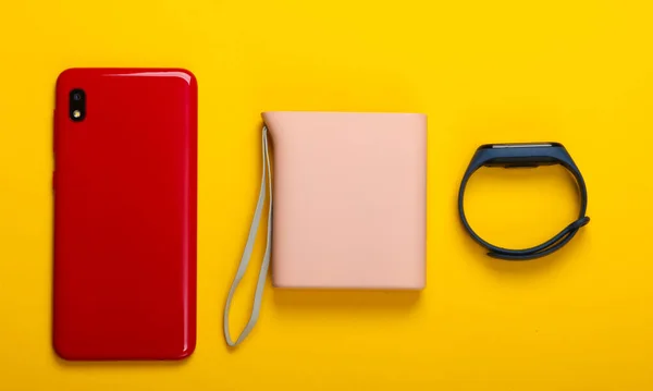 Modern gadgets. Smartphone and smart bracelet, power bank on yellow background. Top view