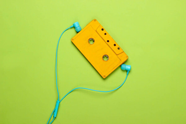 Retro audio cassette with earphones on green pastel background. 80s. Top view. Minimalism.