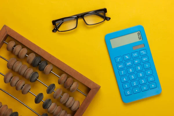 Vintage abacus and calculator, glasses on yellow  background. Top view.