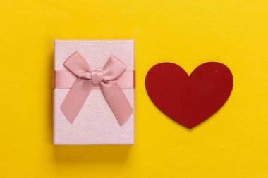 Sarı arka planda fiyonklu ve kalbi olan hediye kutusu. Tatil, Sevgililer Günü. Üst görünüm