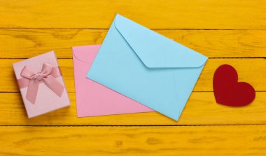 Pembe ve mavi zarf, hediye kutuları, sarı ahşap arka planda kalp. Sevgililer Günü. Üst görünüm