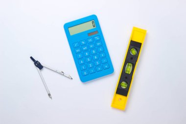 İnşaat seviyesi ve hesap makinesi, beyaz stüdyo arka planında pusula. İnşaat aleti. Üst Manzara. Minimalizm