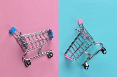Mavi, pembe pastel arka planda iki mini market arabası. Alışveriş konsepti. Üst Manzara. Minimalizm