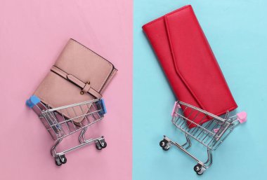 İki küçük market vagonu ve mavi pastel arka planda cüzdanları var. Alışveriş konsepti. Üst Manzara. Minimalizm