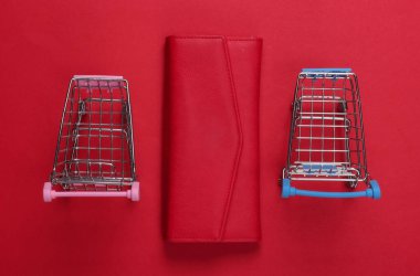 Kırmızı arka planda cüzdanı olan iki mini market arabası. Alışveriş konsepti. Üst Manzara. Minimalizm