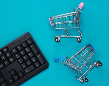 İnternetten alışveriş. Mavi arka planda süpermarket arabaları olan bilgisayar klavyesi. Üst Manzara. Düz yatıyordu 