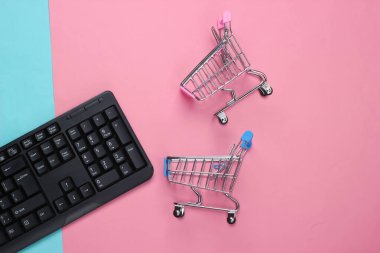 İnternetten alışveriş. Pembe arka planda süpermarket arabaları olan bilgisayar klavyesi. Üst Manzara. Düz yatıyordu 