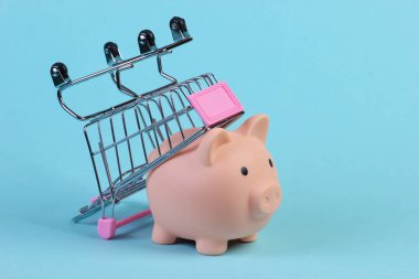 Mavi arka planda domuz kumbarası olan alışveriş arabası.